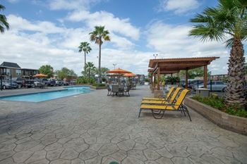 A pool area with a patio, chairs and umbrellas